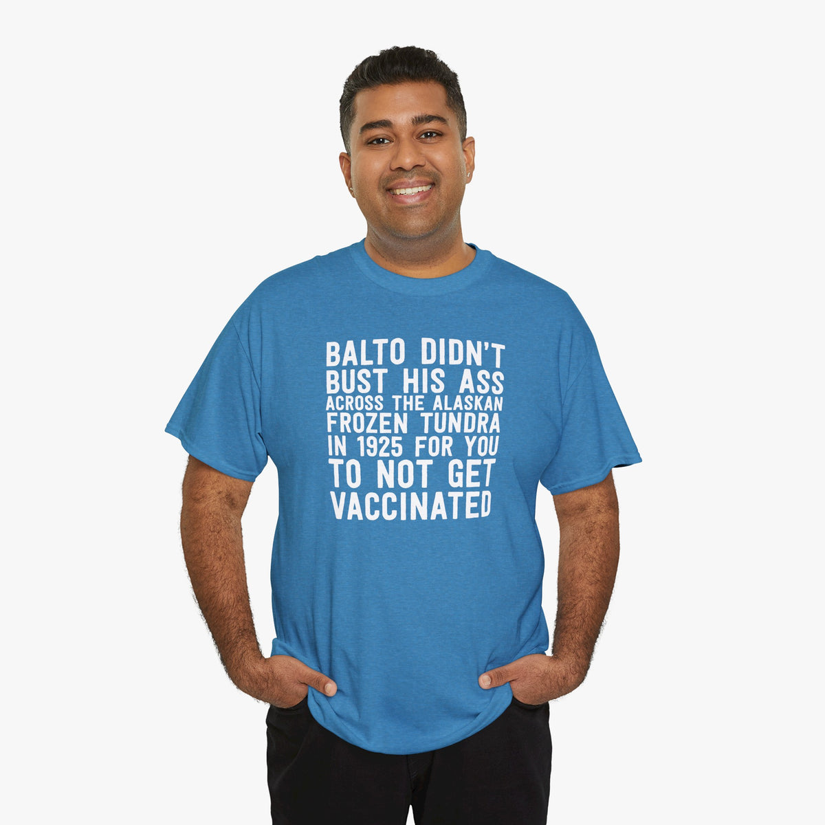 Smiling man with his hands in his pockets wearing a heather blue t-shirt that reads Balto didn't bust his ass across the Alaskan frozen tundra in 1925 for you to not get vaccinated