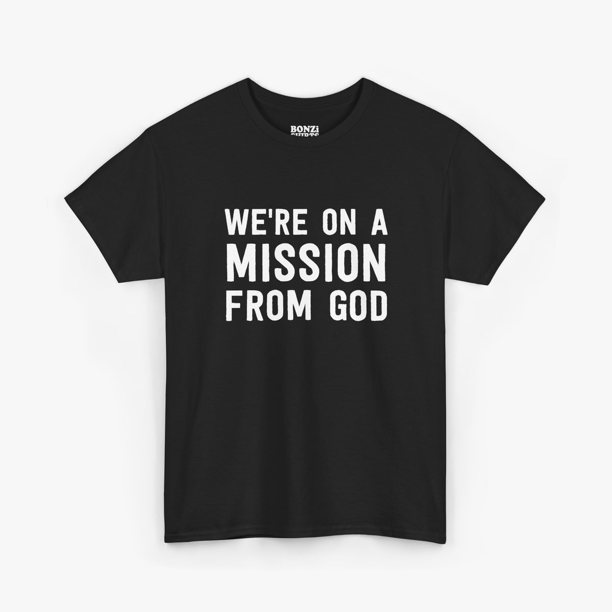 Black t-shirt with bold white text reading We're On A Mission From God across three lines, laid flat on a light gray background